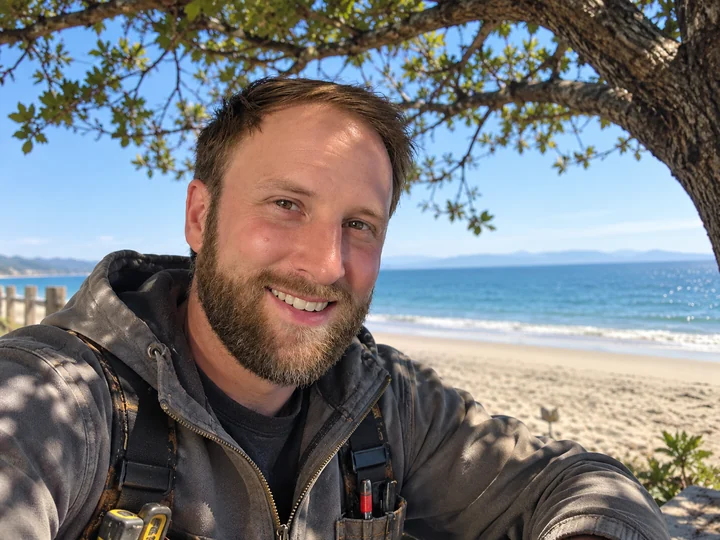Evan smiling in the shade beside the beach.