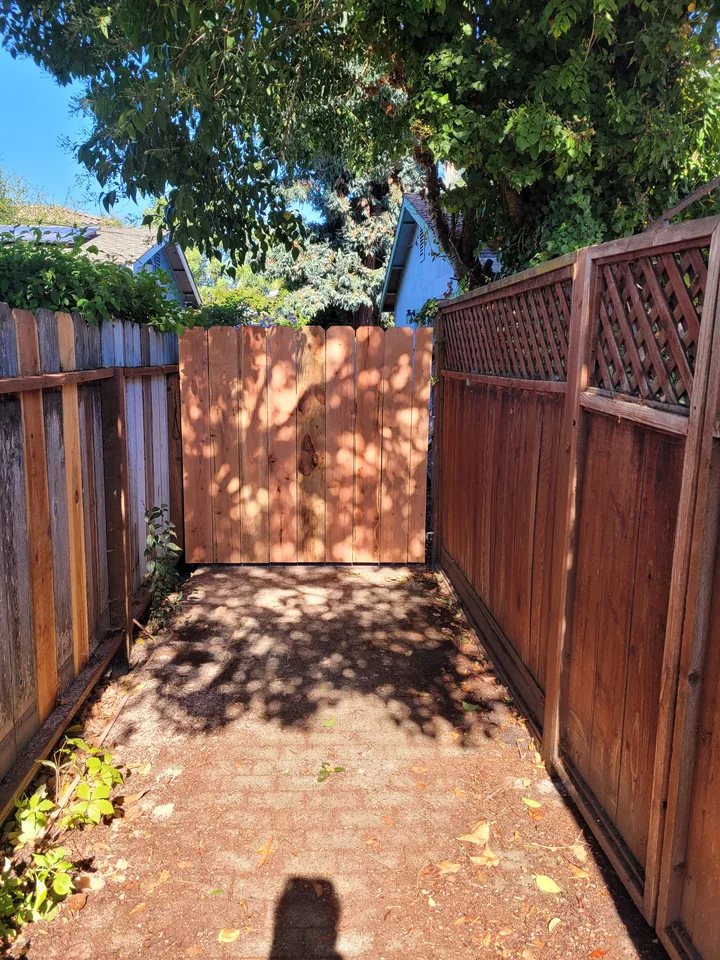 A separate vertical-board wooden gate at the end of a paved passage beside a lattice-topped fence.
