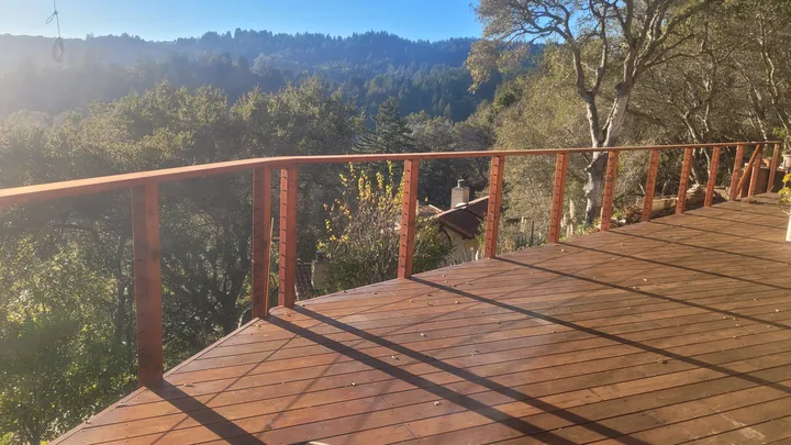 Completed wood-and-cable railing viewed across the deck, with diagonal shadows on the boards.