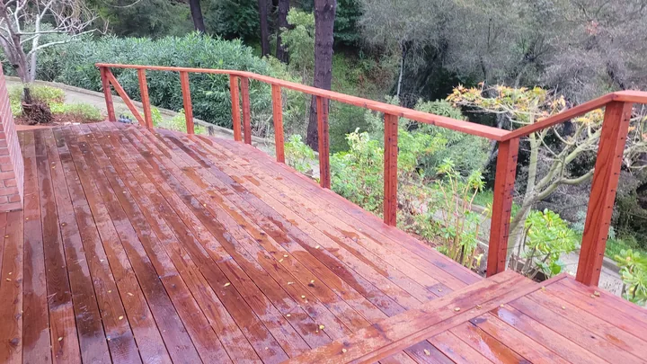 Stained deck railing following a short stair transition above a wooded garden.