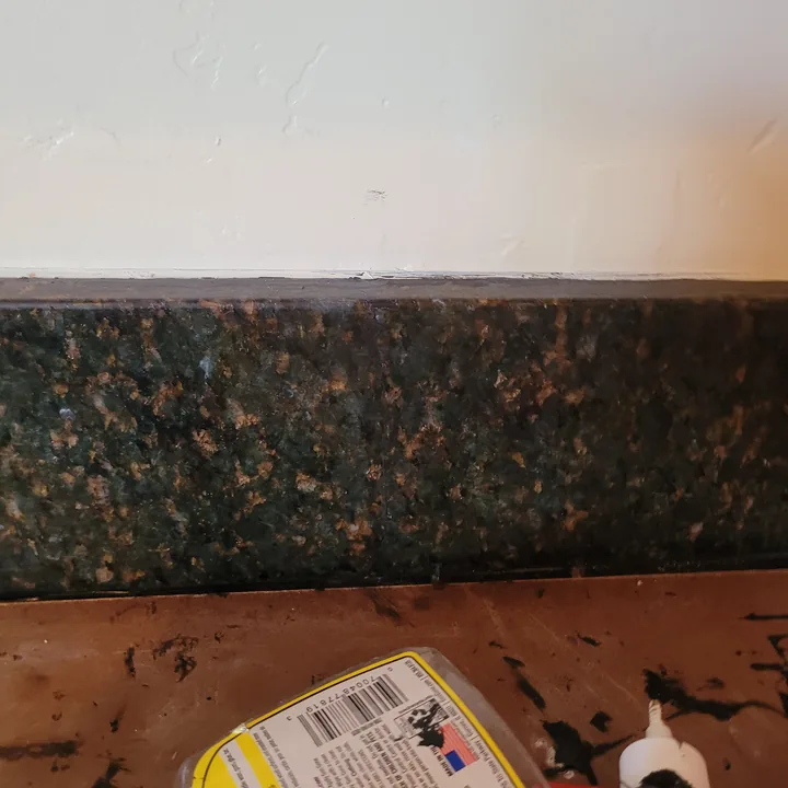 Repaired dark stone backsplash at the previously damaged area, with adjacent wall finishing still in progress.
