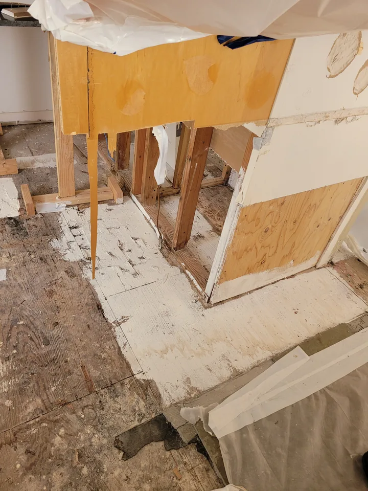 Opened kitchen cabinet and wall areas with exposed framing and unfinished flooring during the repairs.