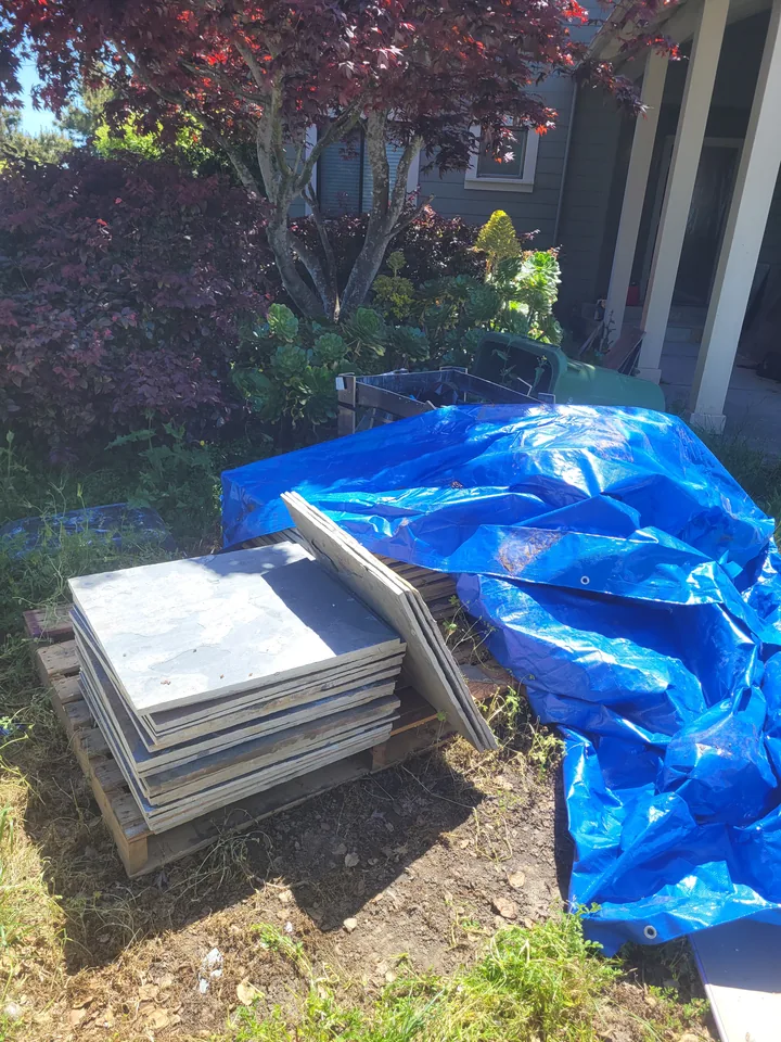 Oversized square replacement tiles stacked outdoors beside a blue tarp before cutting and fitting.