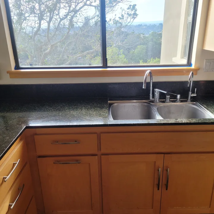 Kitchen window and sink with the custom light wood sill installed and the counter cleared of work tools.