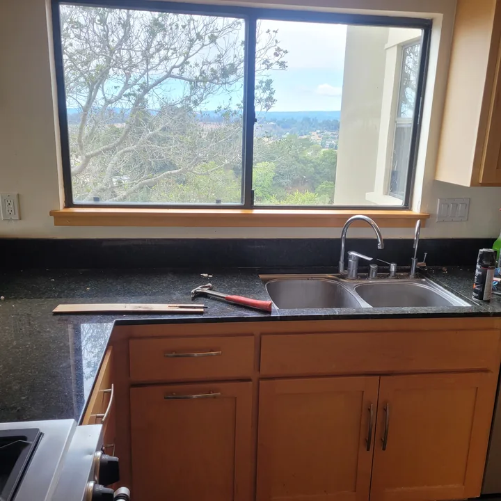 Light wood replacement sill beneath the kitchen window, with tools resting on the dark countertop.