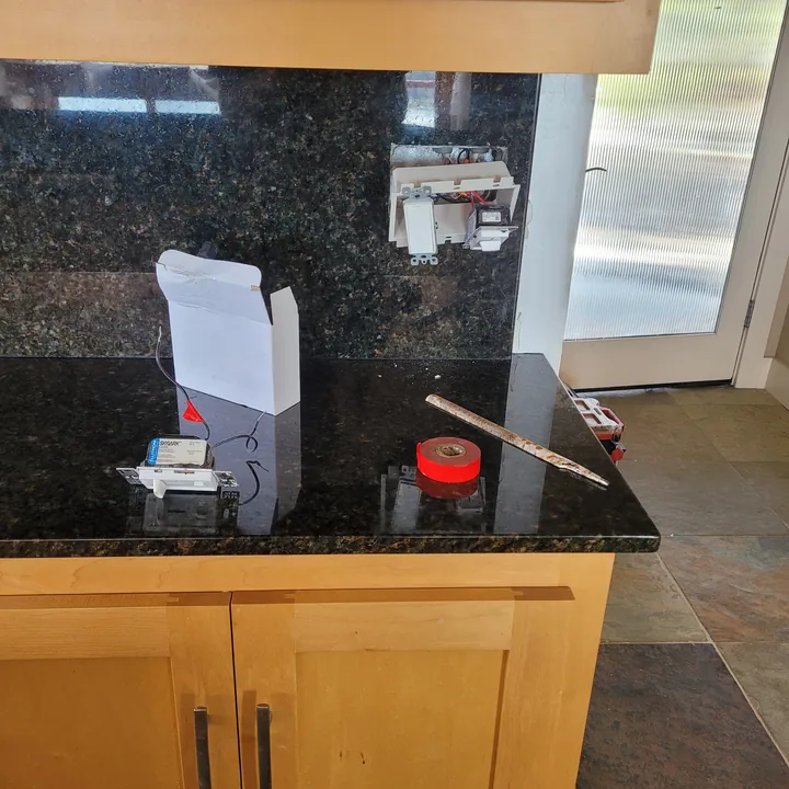 White switch plate back in place against the repaired dark stone backsplash, with work items on the counter.