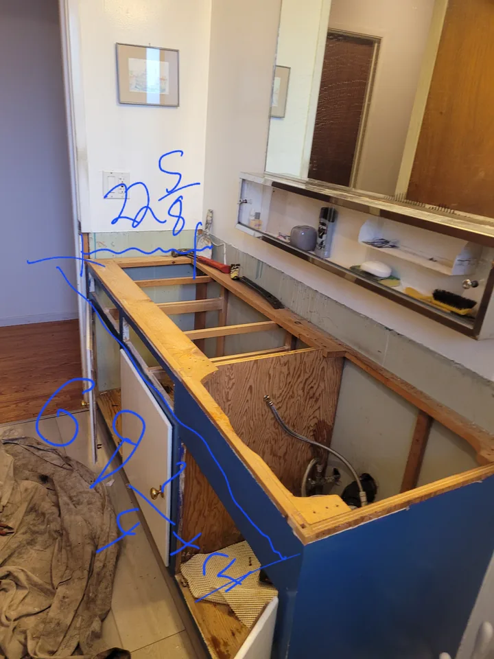 Existing vanity with the old sink and countertop removed, exposing cabinet framing and plumbing.